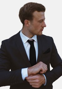 Mustaline ülikond musta jopega, mille all on valge särk ja must lips, lisaks taskurätik. Paremas randmes on stiilne käekell, mis lõpetab välimuse.
