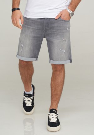 Bermudas de mezclilla gris con puños enrollados, que presentan detalles desgastados y un corte ajustado, combinadas con zapatillas negras y una camiseta blanca.