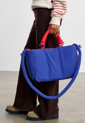Niebieska materiałowa torba z czerwonymi, wyściełanymi rączkami; prostokątny kształt, gładka tekstura i odpinany pasek na ramię. Posiada zapięcie na zatrzask.