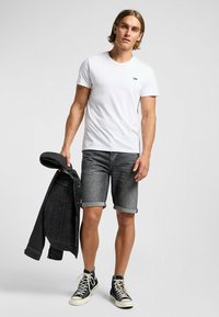 Camiseta blanca de algodón con un pequeño logo negro de "Lee", combinada con pantalones cortos de mezclilla grises y una chaqueta de mezclilla negra, completada con zapatillas negras de caña alta.