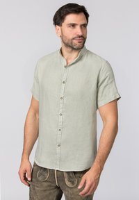 Kurzärmliges, hellgrünes Leinenhemd mit Stehkragen, mit Knopfleiste und subtiler Textur. Getragen mit braunen bestickten Hosen.