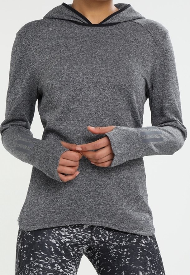 Personne portant un haut à capuche gris à manches longues avec des trous pour les pouces et des leggings noirs à motifs, debout les mains jointes.