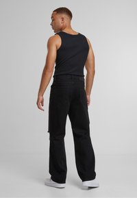 Mustast tankist ja mustad laiad teksad tagant vaadatuna. Valged tossud. Sile kangas, teksadel kerge kulumine. Lihtne disain.