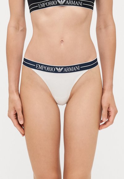 Balts tanga apakšbikses ar tumši zilu elastīgo jostu, uz kuras ir redzams "Emporio Armani" logo. Gluda auduma un minimālisma griezuma dizains.