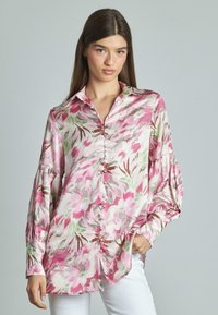 Blusa a maniche lunghe leggermente stampata, nei colori rosa, bianco e verde, con una texture liscia e setosa, dotata di chiusura con bottoni e colletto.