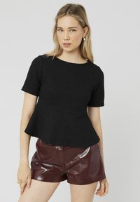 Top peplum noir en tissu côtelé avec des manches courtes et un col rond, associé à un short bordeaux brillant.