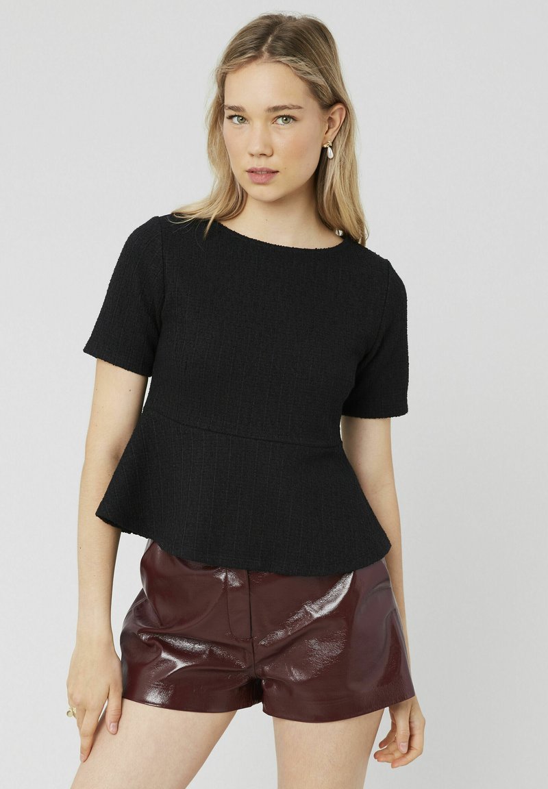 Top peplum noir en tissu côtelé avec des manches courtes et un col rond, associé à un short bordeaux brillant.