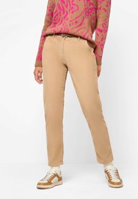 Pantalon en velours côtelé beige à coupe droite avec poches devant, assorti à des baskets marron et crème, et un pull à motifs rose et marron.