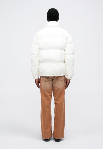 Giacca piumino bianca con colletto alto, caratterizzata da un design trapuntato. Abbinata a jeans larghi marrone chiaro sbiaditi. Colore uniforme in tutta la giacca.