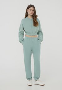 Sweatshirt verde chiaro corto con zip e maniche lunghe abbinato a pantaloni jogger coordinati con vita elastica e orli a costine.