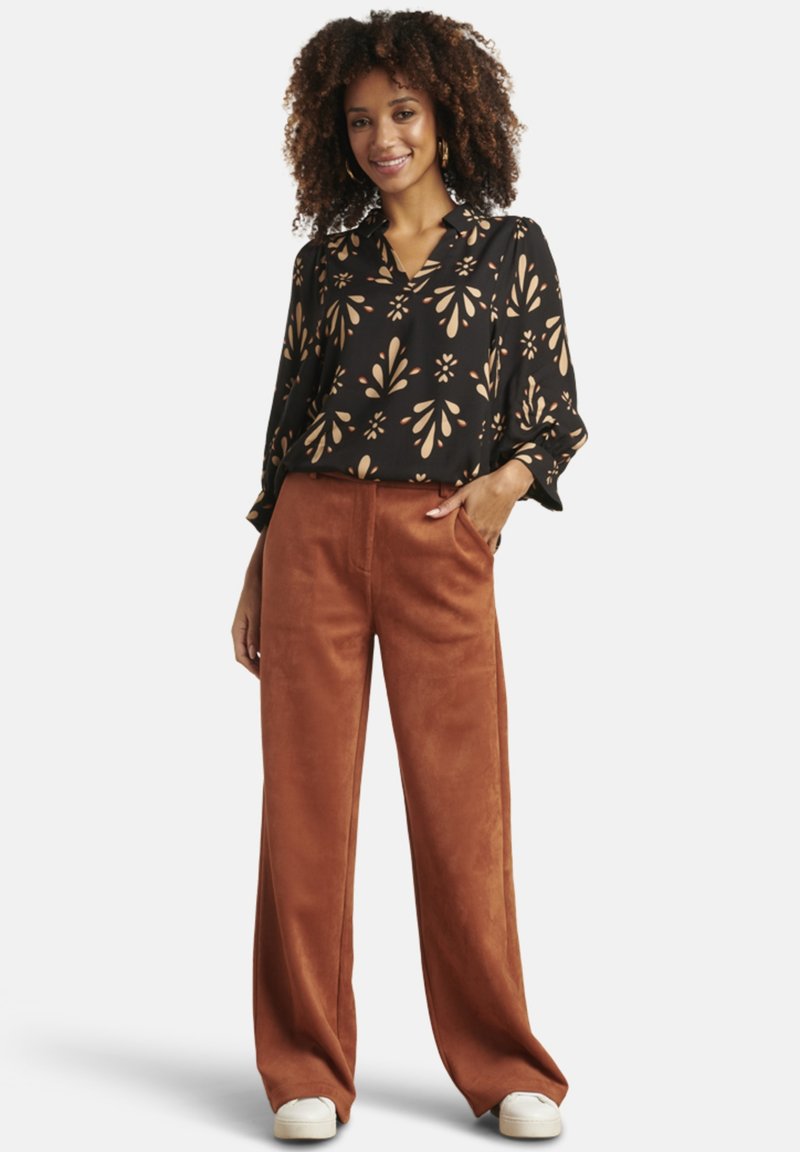 Black blouse with beige floral pattern and wide sleeves, paired with brown wide-leg trousers. Model wears white sneakers.