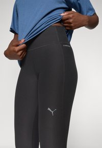 Crne sportske tajice s visokim strukom, s detaljima šivanja i malim sivim Puma logom na lijevom bedru. Glatka tekstura.