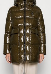 Abrigo acolchado brillante de color verde oliva con capucha, que cuenta con un cierre de cremallera, dos bolsillos frontales y un diseño acolchado. Textura suave y acabado brillante.