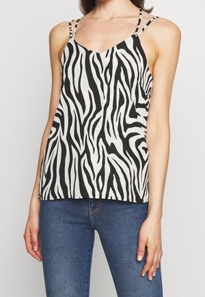 Kobieta ubrana w czarno-biały bezrękawnik w nadruk zebry z cienkimi ramiączkami i niebieskie dżinsy, pokazana od szyi do bioder.