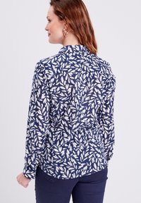 Camicia blu navy con motivo a foglie bianche, maniche lunghe, colletto e polsini con bottoni, realizzata in un tessuto morbido con una finitura leggermente testurizzata.