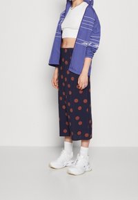 Chaqueta azul con cremallera y rayas blancas, top blanco corto, falda de lunares azul marino y zapatillas blancas con suelas texturizadas y calcetines hasta el tobillo.