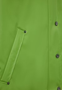 Světlá zelená nepromokavá bunda s hladkým povrchem, velkou boční kapsou a černými patentky.