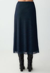 Een donkerblauwe rok van een transparante, gestructureerde stof met een subtiel zebra-patroon, vallend tot halverwege de kuit, gecombineerd met zwart kniehoge laarzen.