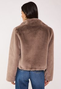 Veste en fausse fourrure marron avec col montant, forme carrée et manches longues. Caractérisée par une texture douce et un design épuré sans ornements.