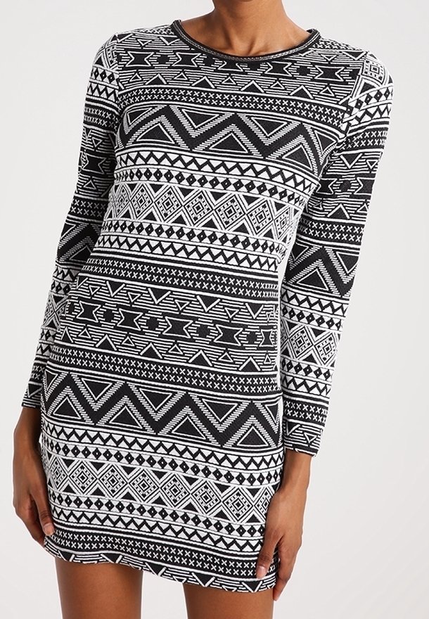 Femme portant une robe à manches longues, noire et blanche avec des motifs tribaux géométriques et un col rond.