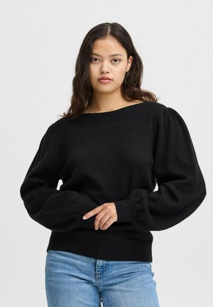 Pull en tricot noir avec un large col bateau, des manches longues bouffantes et des bords côtelés au niveau des poignets et de l'ourlet. Assorti à un jean bleu clair.
