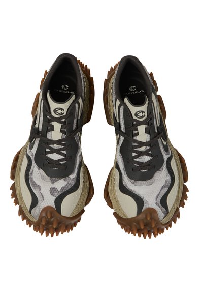 Paire de baskets blanches, noires et beiges avec semelles marron texturées à picots et lacets noirs, vues de dessus sur un fond blanc.