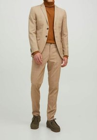 Beige rutigt kostym med en skräddarsydd kavaj, matchande slim-fit byxor och brun polotröja, tillsammans med mörkbruna skor.