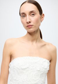 Strapless white dress featuring intricate floral appliqué and a smooth satin finish. Model displays a neutral background.