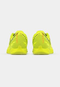 Lysegule atletiksko med en tekstureret mesh-overdel, der har sorte accenter og en fleksibel gummisål designet til forbedret greb.