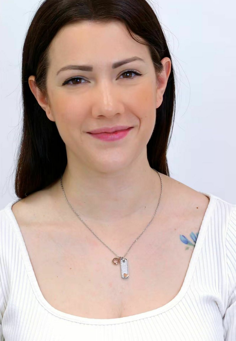 Collana d'argento con pendente testurizzato e ciondolo circolare, indossata su un top bianco a coste, su uno sfondo uniforme.