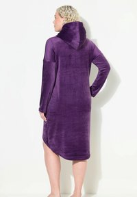 Violetti hupparimekko, joka on valmistettu pehmeästä, samettimaisesta materiaalista. Mekossa on pitkät hihat ja hieman epäsymmetrinen helma. Sileä pinta ja moderni muotoilu.
