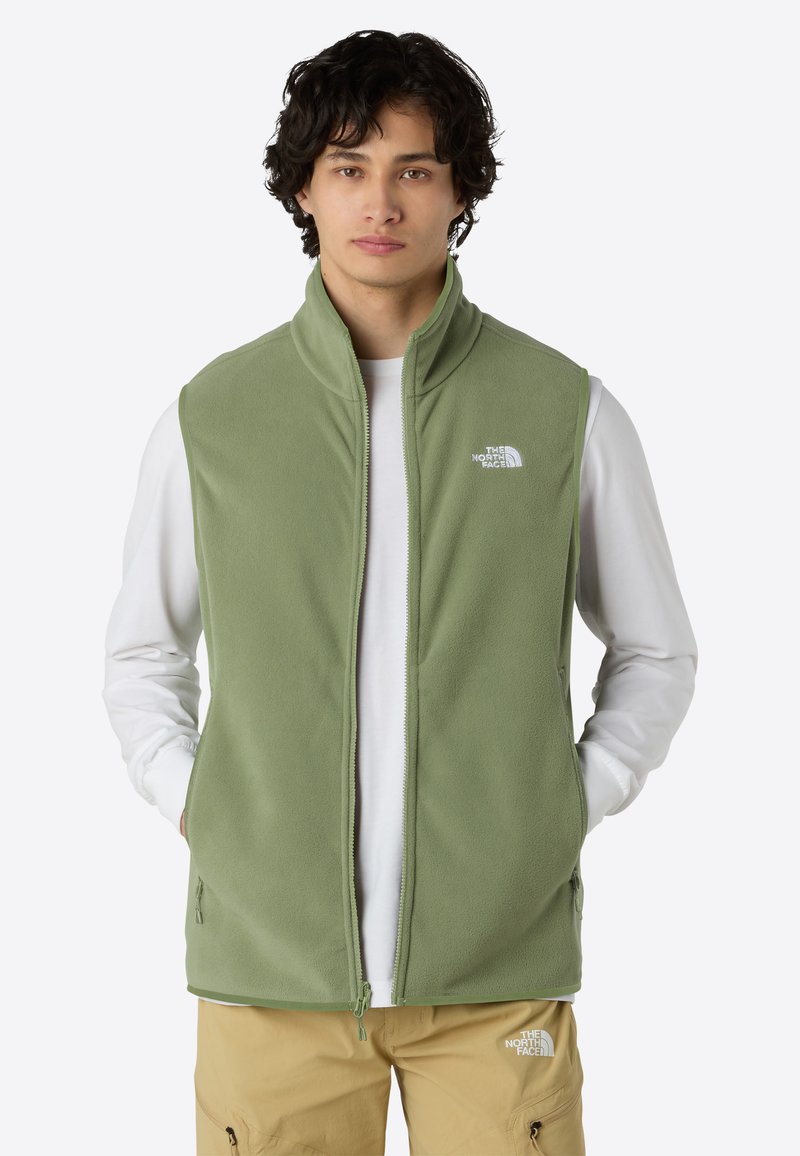 Grüner Fleece-Weste mit hohem Kragen, Frontreißverschluss und zwei Seitentaschen. Verfügt über ein kleines weißes Logo auf der linken Brust. Getragen über einem weißen Langarmshirt.