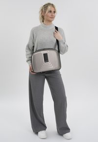 Metalen grijze schoudertas met gestructureerde horizontale ribbels, zwarte accenten en een centraal logo. Verstelbare riem voor crossbody-dragen.