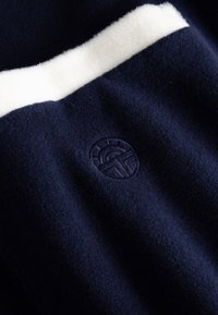Marineblaue Fleece-Stoff mit weißem Wollakzent und einem gestickten Logo, das eine weiche Textur und ein klares Design zeigt.