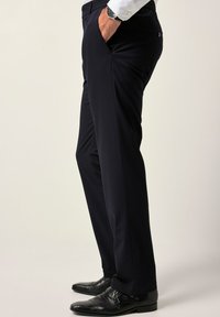 Pantaloni navy in tessuto liscio, con tasche laterali e passanti per cintura. Abbinati a scarpe nere, che mostrano un design elegante e una vestibilità su misura.