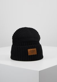 Mustat ribbed-kudotut pipo, jossa on taitettu huppu ja suorakulmainen ruskea nahkalappu, jossa on "Timberland Company" -logo.