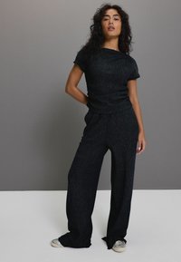 Schwarzes gestricktes Zweiteiler-Outfit mit einem kurzärmligen Oberteil und weiten Hosen. Weiche Textur mit einem dezenten Muster, kombiniert mit hellen Schuhen.