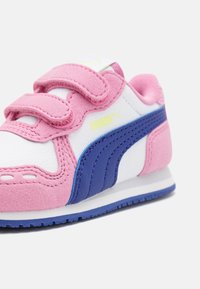 Rosa och vita sneakers i mocka och läder, med kardborreband och ett blått rand längs sidan, prydda med en gul logotyp.