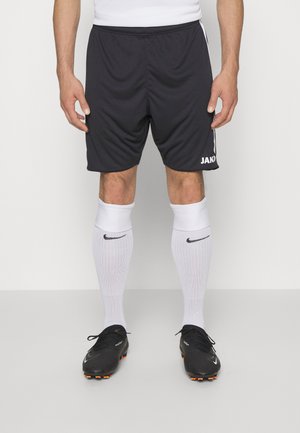 Schwarze Sportshorts mit Gummibund, kombiniert mit weißen, knielangen Socken mit einem schwarzen Nike-Logo und schwarzen Fußballschuhen.