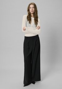 Light beige long-sleeve sweater with a textured finish and blue patterned accents, paired with black wide-leg trousers and pointed black shoes.