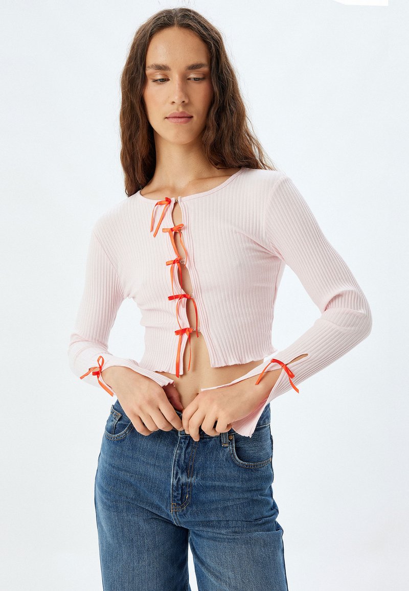 Helles rosa, geripptes Langarmoberteil mit orangen Bandbändern an der Vorderseite und den Ärmeln, cropped Design und rohem Saum.