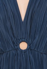 Jūras flotes krāsas svārku kleita ar dziļu V veida kakla izgriezumu un apaļu izgriezumu vidukļa daļā, ko ieskauj savelkta auduma daļa. Zīdaina tekstūra.