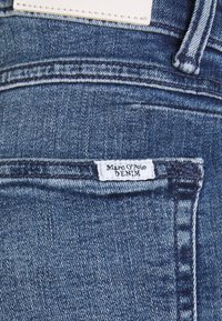 Dunkelblaue Jeans aus Denim mit einer strukturierten Oberfläche, ausgestattet mit einem weißen Etikett, das auf den Bund genäht ist und "Marc O'Polo DENIM" liest.