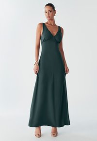 Tumeroheline maksikleit sügava V-kaelusega, keha järgiva ülalt ja voolava seelikuga. Kangas on sile ja kergelt läikiv. Omab õhukesi õlapaelu.