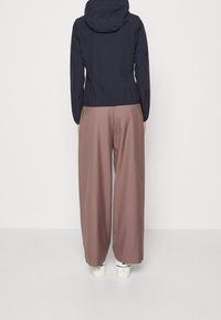 Granatowa kurtka z kapturem o dopasowanej talii, zestawiona z luźnymi, jasnobrązowymi spodniami. Obie części garderoby mają gładką fakturę i minimalistyczne detale.