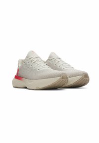 Beige sneakers with a textured knit upper, light cushioning, and a red accent on the heel. Flat rubber sole with a patterned tread.
