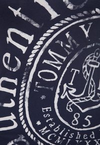Námořnicky modré tričko s velkým bílým grafikou, která obsahuje text, kotvu a detaily lana, vyrobené z měkké bavlny.