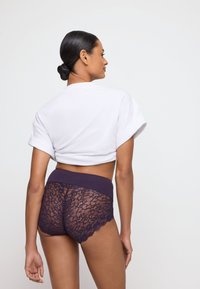 Lace shorts in donkergroen met een brede tailleband en gekartelde randen, gecombineerd met een cropped wit t-shirt, dat de intrigerende kanttextuur toont.