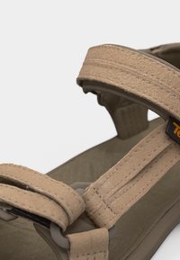 Κοντινό πλάνο μπεζ εξωτερικού σανδάλιου με ρυθμιζόμενους ιμάντες και ανθεκτική σόλα σε λευκό φόντο.