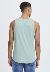 Lys grønn tanktop med rund halslinning og dypere nederkant. Stoffet har en jevn tekstur, uten synlige mønstre eller detaljer.